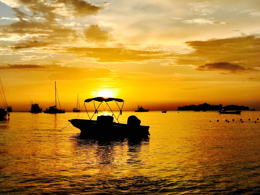 Photo of the sunset over the ocean with a small motor boat silhouetted in the foreground. 